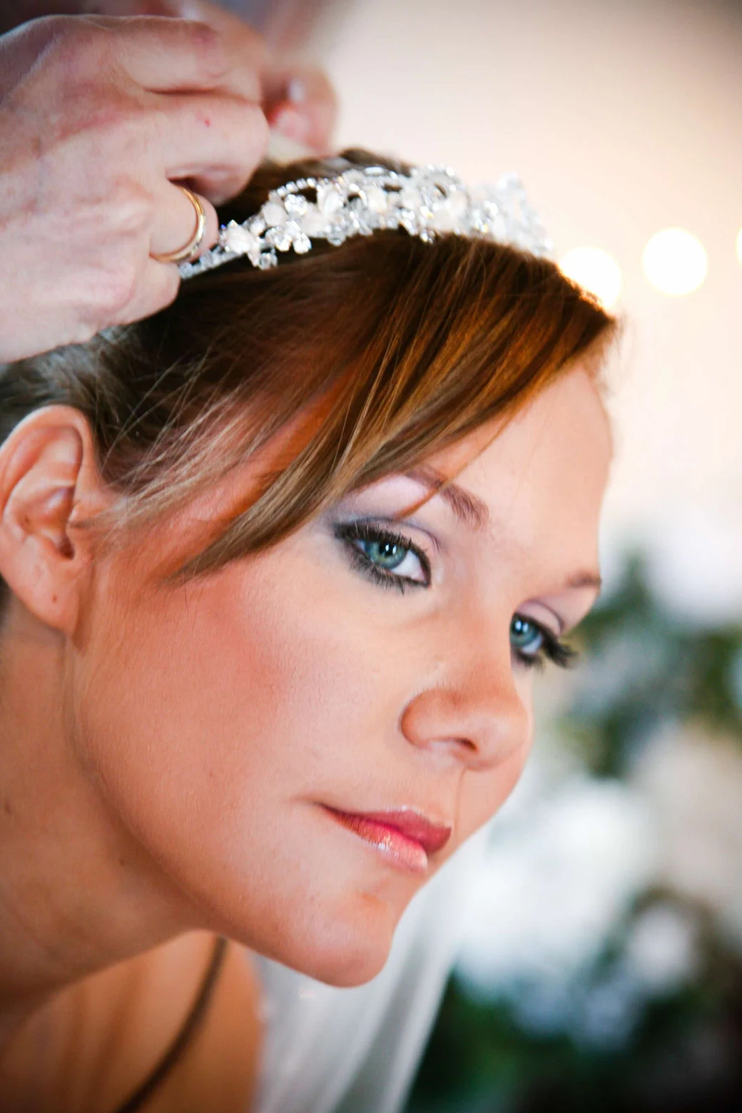 A bride having a tiara placed in her hair after makeup application